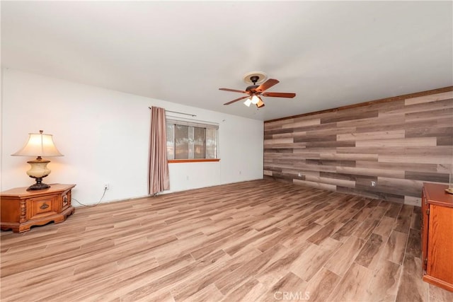 unfurnished living room featuring ceiling fan, wooden walls, and light hardwood / wood-style flooring