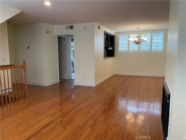 empty room with baseboard heating, light hardwood / wood-style floors, and a notable chandelier