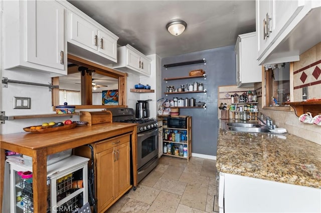 kitchen with white cabinets, light stone counters, backsplash, and gas range