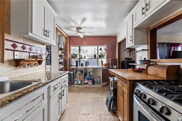 kitchen featuring stainless steel range with gas cooktop, dark stone countertops, white cabinetry, and backsplash