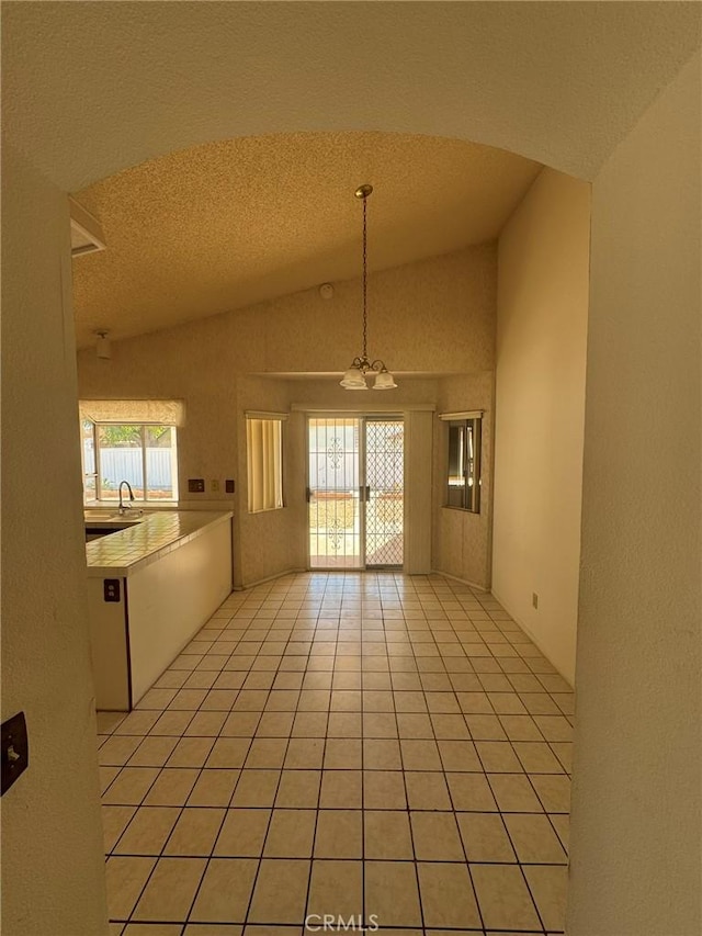 tiled empty room with a textured ceiling, an inviting chandelier, vaulted ceiling, and sink