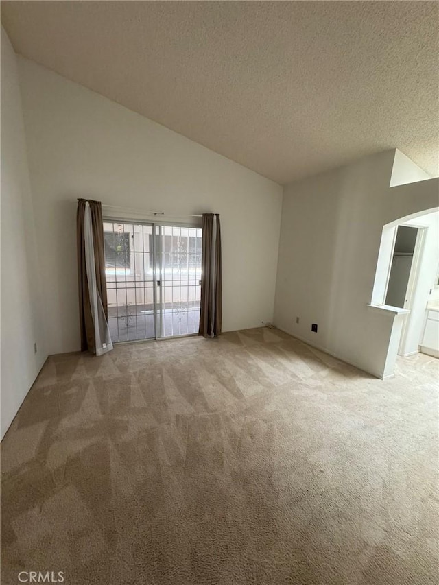 unfurnished room featuring vaulted ceiling, light colored carpet, and a textured ceiling