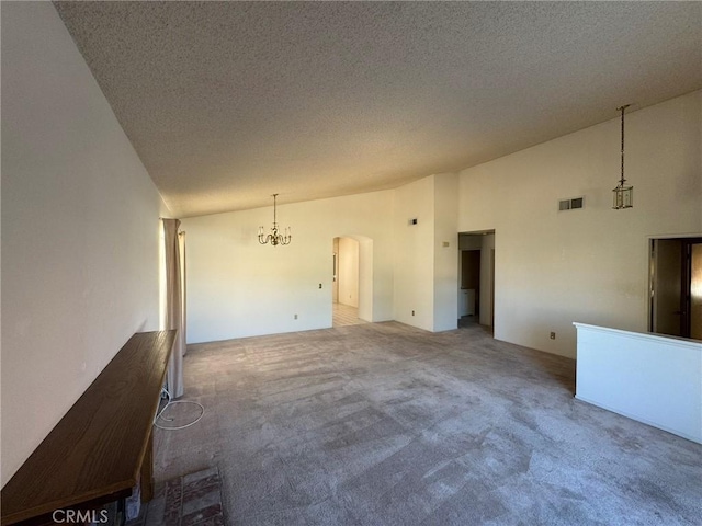 spare room featuring carpet flooring, a notable chandelier, a towering ceiling, and a textured ceiling