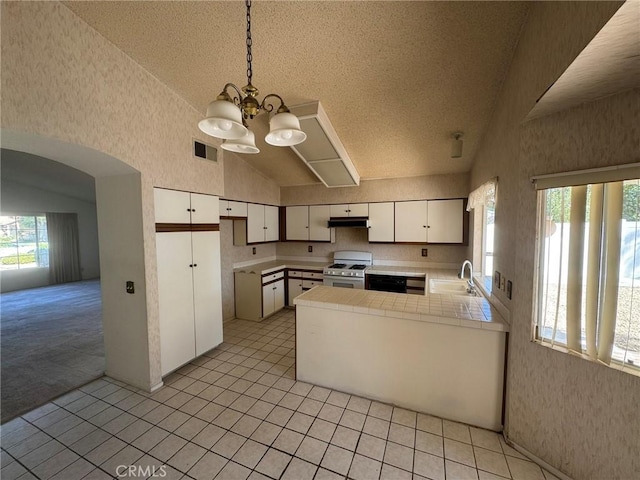 kitchen featuring kitchen peninsula, white gas range, an inviting chandelier, white cabinets, and hanging light fixtures