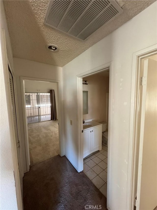 hallway featuring a textured ceiling, light colored carpet, and sink