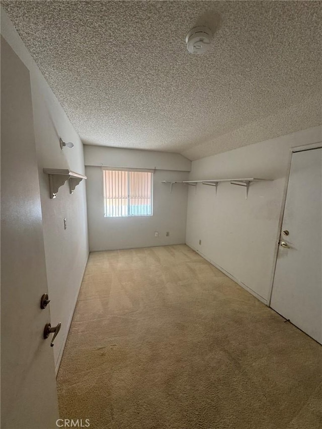 empty room with a textured ceiling, lofted ceiling, and light carpet