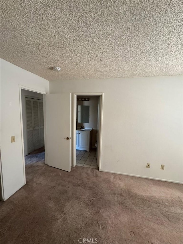 unfurnished bedroom with carpet flooring, a textured ceiling, and connected bathroom