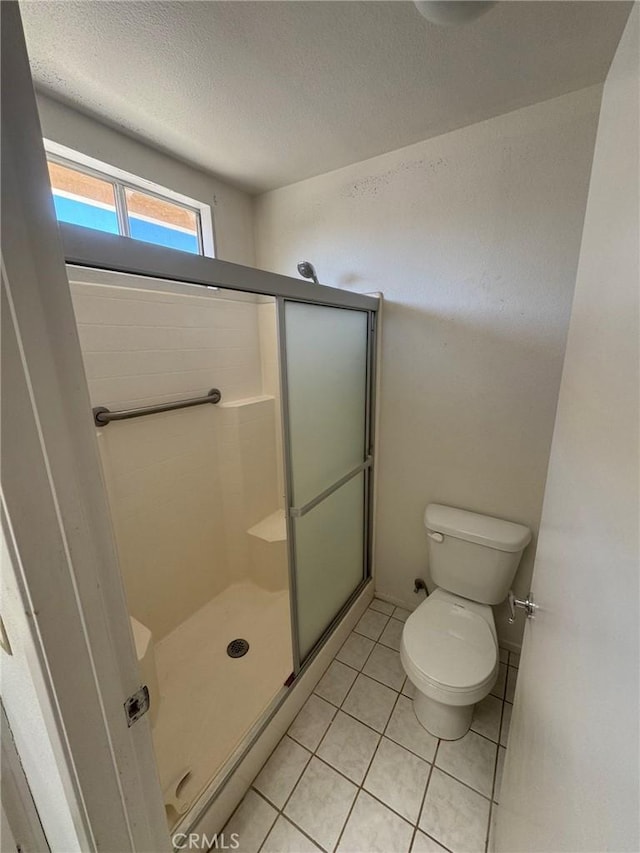 bathroom with toilet, a textured ceiling, tile patterned floors, and a shower with door