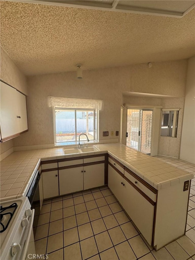 kitchen featuring white cabinetry, sink, white range oven, tile countertops, and kitchen peninsula