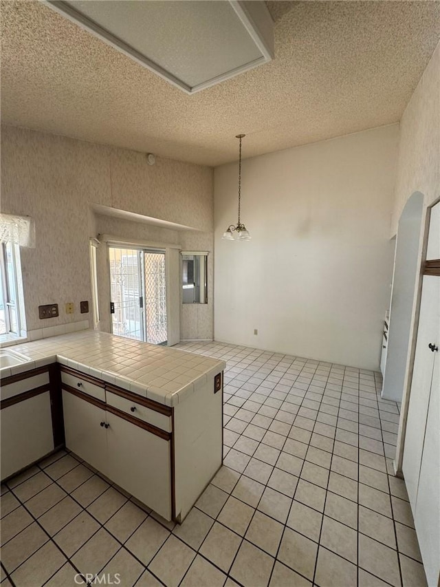 kitchen with tile countertops, kitchen peninsula, white cabinets, and a textured ceiling