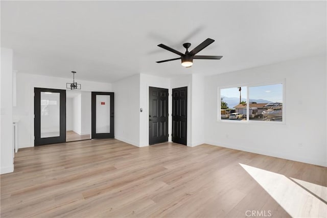 empty room with ceiling fan with notable chandelier, light wood-type flooring, and french doors