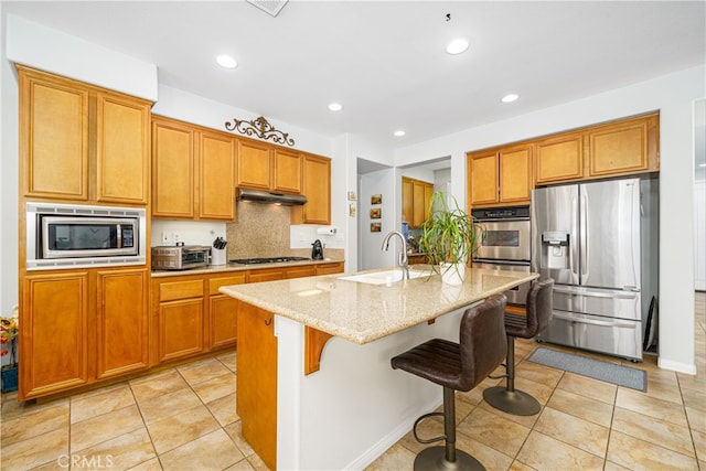 kitchen featuring sink, a kitchen island with sink, a breakfast bar area, light stone countertops, and stainless steel appliances