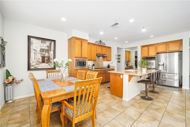 kitchen featuring stainless steel appliances, a kitchen breakfast bar, backsplash, a center island with sink, and light tile patterned floors