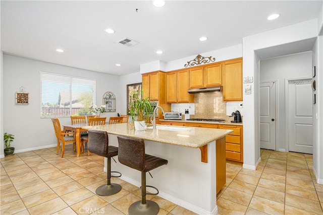 kitchen with sink, an island with sink, light tile patterned floors, backsplash, and light stone countertops