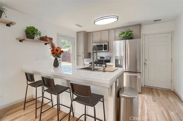 kitchen with kitchen peninsula, tile countertops, light wood-type flooring, gray cabinets, and stainless steel appliances