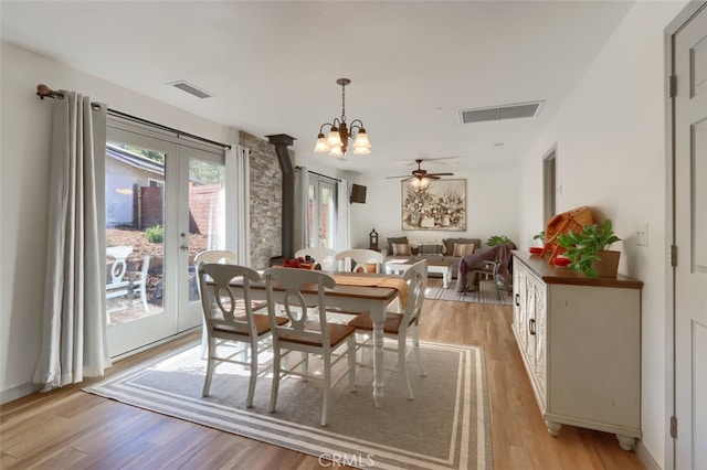 dining area with a wood stove, light wood-type flooring, and ceiling fan with notable chandelier