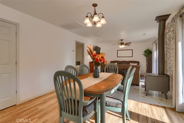 dining area featuring a wood stove, ceiling fan with notable chandelier, and light wood-type flooring