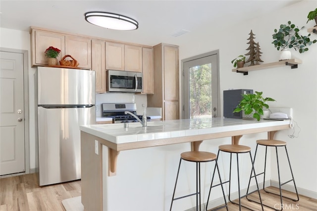 kitchen with kitchen peninsula, a breakfast bar area, stainless steel appliances, tile counters, and light hardwood / wood-style flooring