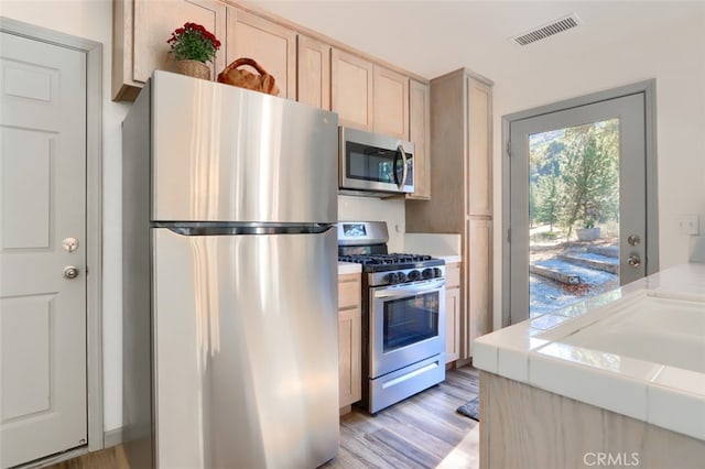 kitchen featuring light brown cabinetry, appliances with stainless steel finishes, light hardwood / wood-style flooring, and tile counters