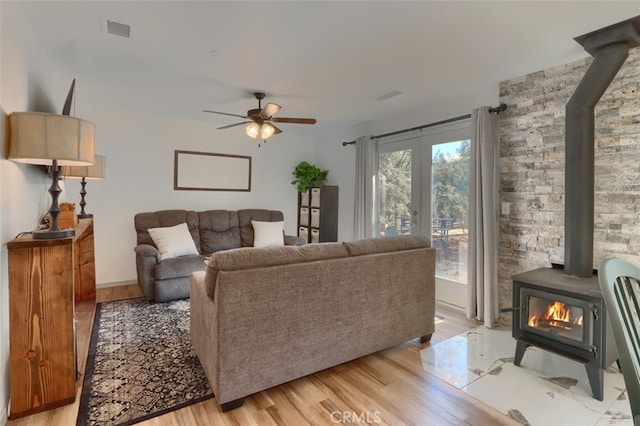 living room with light hardwood / wood-style flooring, a wood stove, and ceiling fan