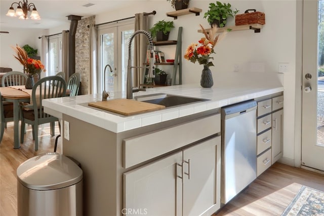 bar featuring sink, light hardwood / wood-style floors, dishwasher, and tile counters