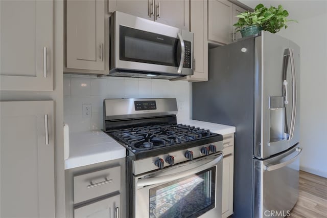 kitchen featuring gray cabinetry, backsplash, stainless steel appliances, and light wood-type flooring