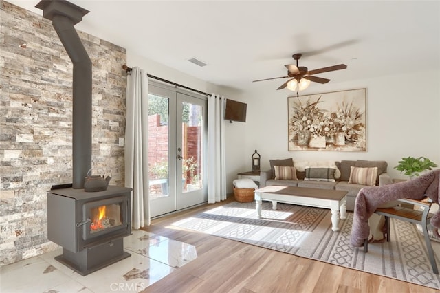 living room with french doors, light hardwood / wood-style floors, a wood stove, and ceiling fan