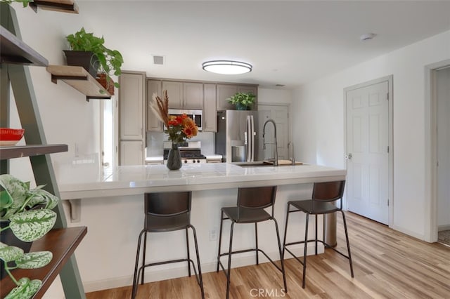 kitchen featuring light hardwood / wood-style flooring, appliances with stainless steel finishes, sink, gray cabinets, and a breakfast bar