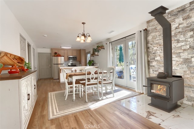 dining space with a chandelier, light wood-type flooring, a wood stove, and french doors