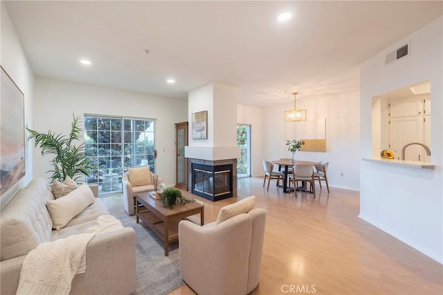 living room with a multi sided fireplace, a chandelier, sink, and light wood-type flooring