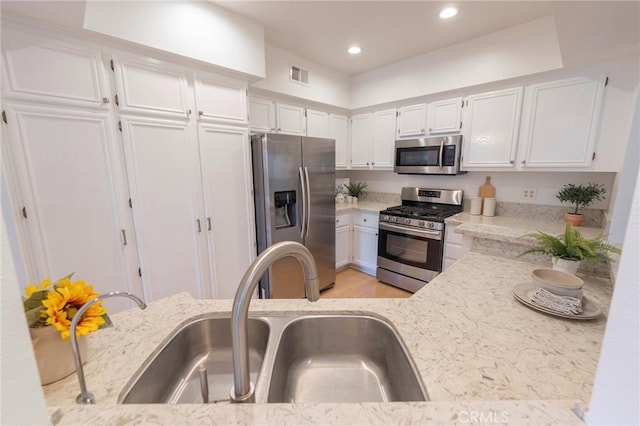 kitchen with white cabinetry, stainless steel appliances, sink, and light stone counters