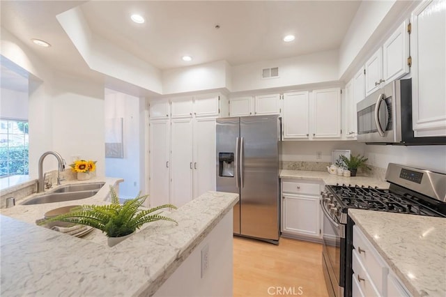 kitchen featuring appliances with stainless steel finishes, white cabinetry, sink, light hardwood / wood-style floors, and light stone countertops