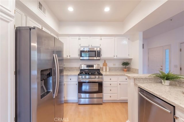 kitchen with appliances with stainless steel finishes, light stone countertops, light hardwood / wood-style floors, and white cabinets