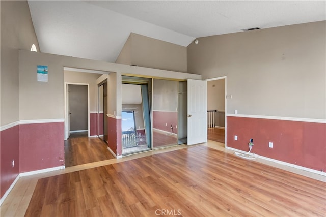 unfurnished bedroom featuring hardwood / wood-style floors, high vaulted ceiling, and a closet