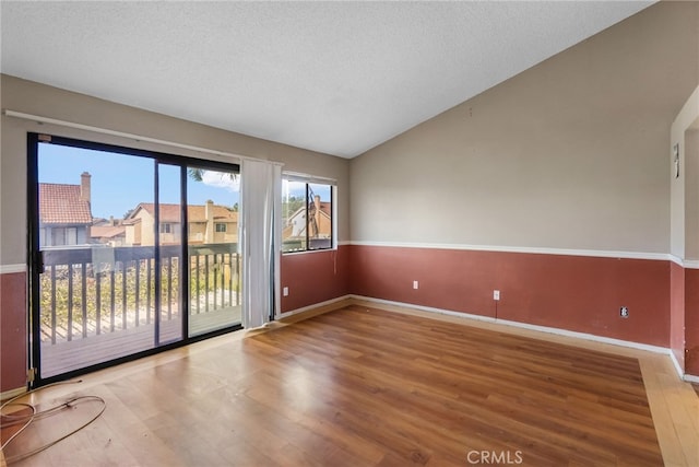 empty room featuring a textured ceiling, hardwood / wood-style floors, and lofted ceiling