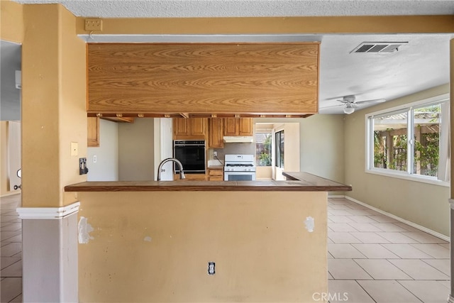 kitchen with kitchen peninsula, light tile patterned floors, white range with gas cooktop, and ceiling fan