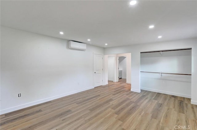 unfurnished bedroom with a wall mounted air conditioner and light hardwood / wood-style flooring