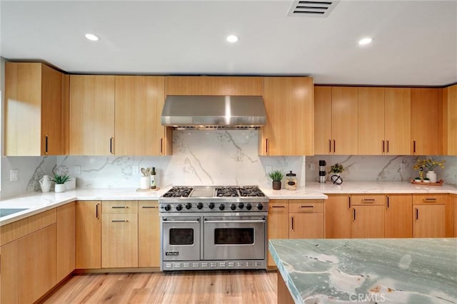 kitchen with tasteful backsplash, light hardwood / wood-style flooring, wall chimney exhaust hood, and double oven range