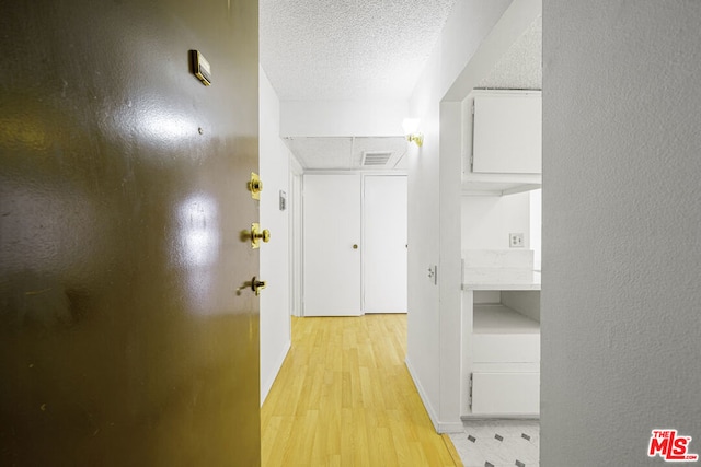 hallway with light hardwood / wood-style floors and a textured ceiling