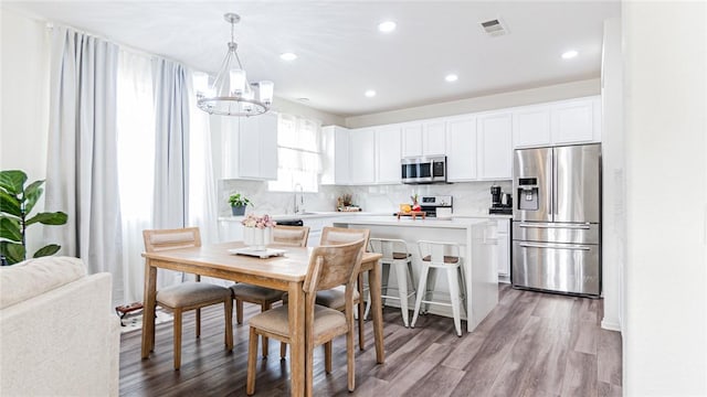 kitchen featuring white cabinets, appliances with stainless steel finishes, light hardwood / wood-style flooring, and hanging light fixtures