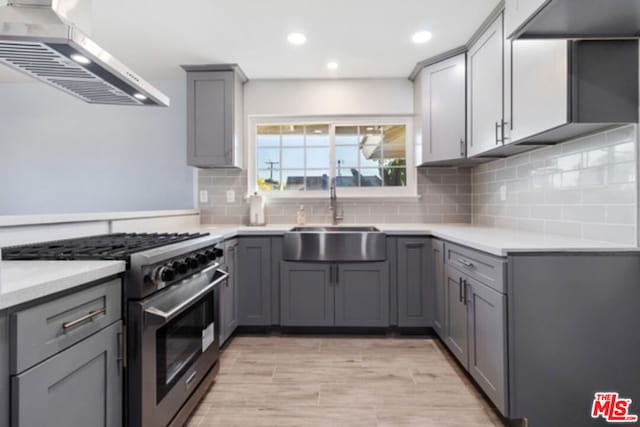 kitchen with gray cabinetry, sink, wall chimney range hood, high end range, and light wood-type flooring