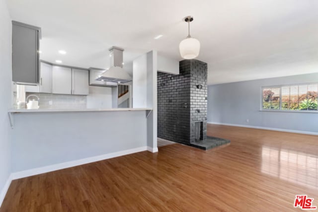 kitchen featuring decorative backsplash, gray cabinets, light wood-type flooring, range hood, and kitchen peninsula