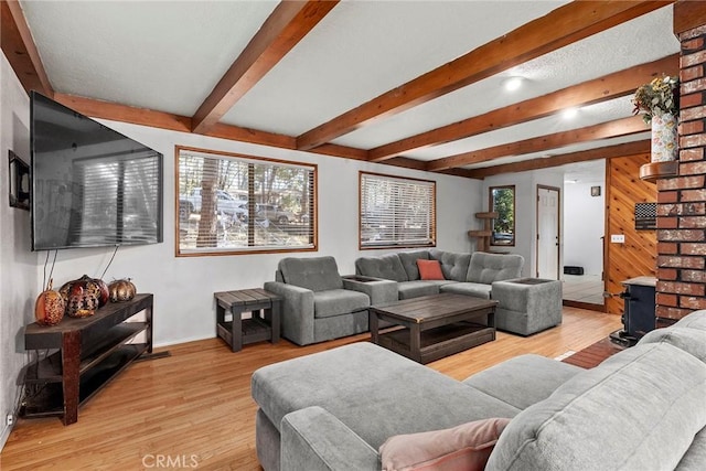 living room featuring a wood stove, light hardwood / wood-style flooring, and beamed ceiling