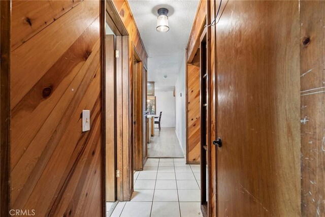 hallway featuring wooden walls and light tile patterned floors