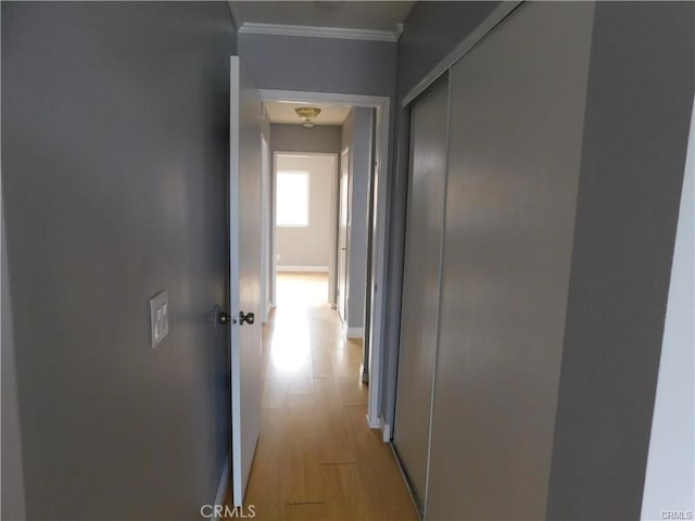 hallway featuring light wood-style floors, baseboards, and ornamental molding