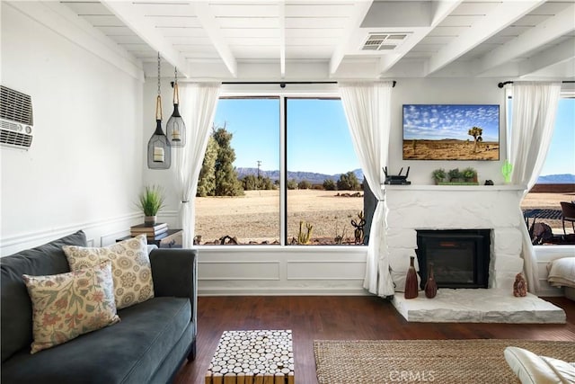 living room featuring beamed ceiling, wooden ceiling, a stone fireplace, and dark wood-type flooring