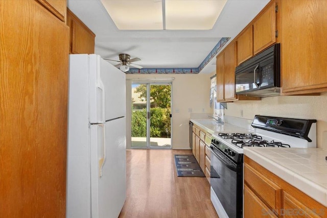 kitchen with ceiling fan, tile countertops, light wood-type flooring, gas range oven, and white fridge