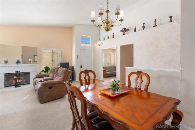 carpeted dining room featuring high vaulted ceiling, a chandelier, and a fireplace