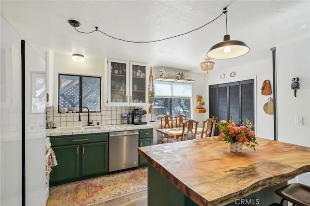 kitchen with light wood-type flooring, backsplash, stainless steel dishwasher, sink, and green cabinetry