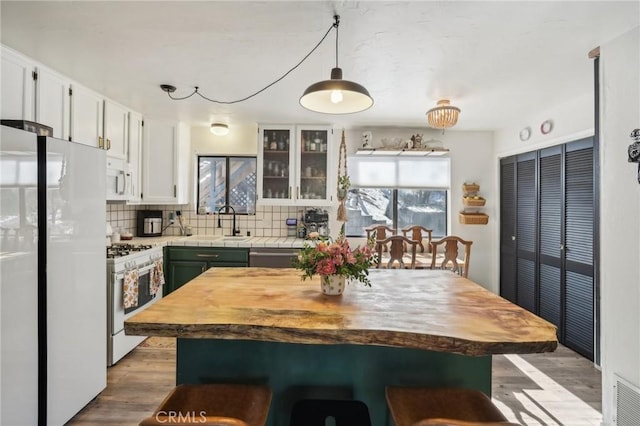 kitchen with light wood-type flooring, tasteful backsplash, white appliances, decorative light fixtures, and white cabinetry